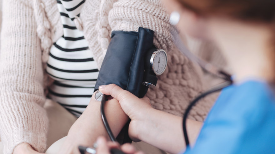 Close up view on a female nurse sitting in front of a senior patient while measuring her blood pressure during a regular visit.