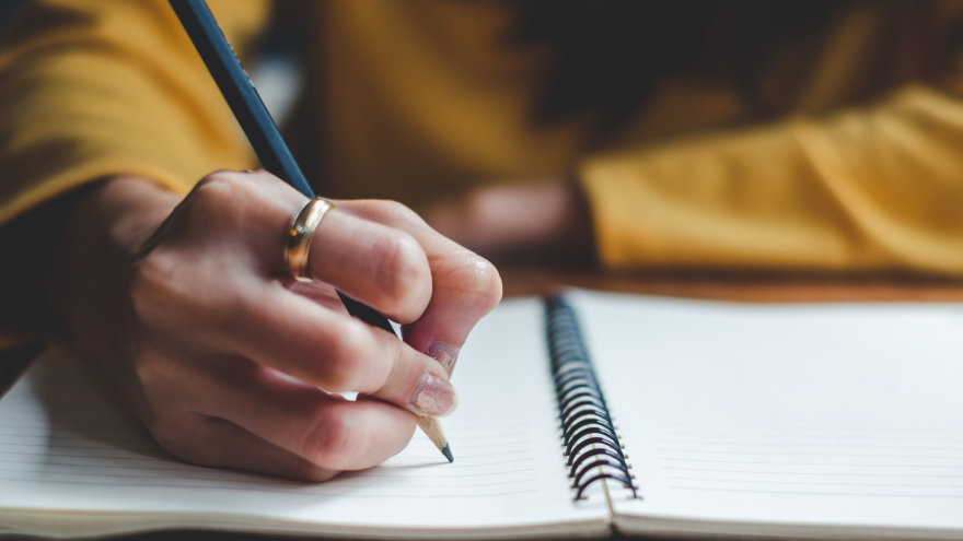 A woman's hand preparing to write on an opened notebook.